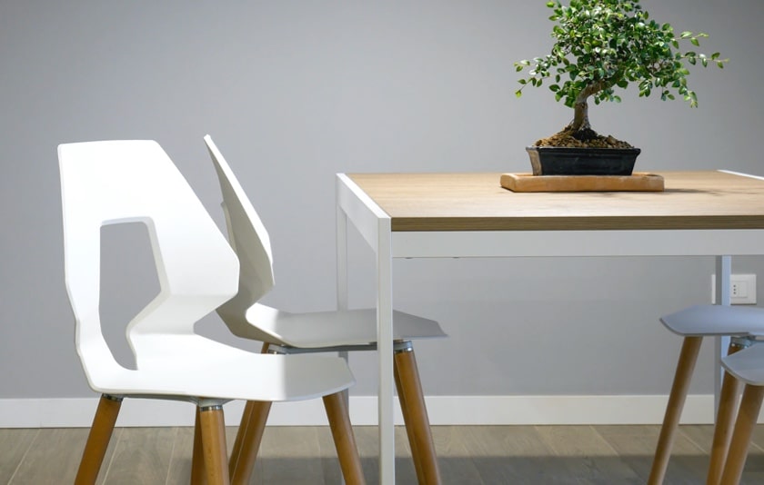 Some white chairs with a table in between having a small plant pot above it.